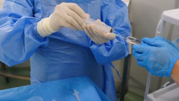 Подготовка к сосудистой хирургии в современной клинике. Профессиональные врачи в хирургических халатах и перчатках готовят препараты для удаления тромба из артерии в больнице. Использование контрастной жидкости для обследования — стоковое видео