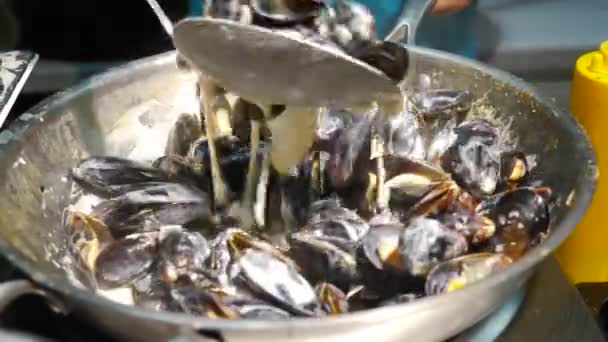 Pouliční jídlo. Vařit míchání čerstvých lahodných mušlí ve skořápkách v kotli s omáčkou. Prodej pouliční stravy na místním trhu nebo festivalu. Středomořská kuchyně. Smažení na velké pražící pánvi — Stock video