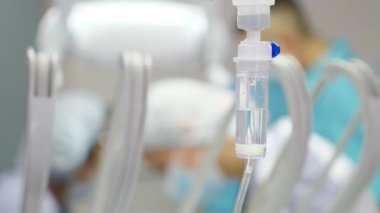 Modern dişçilikte cerrahi operasyon sırasında bulanık dişçiler. Klinikte ameliyat, anestezi altında hasta, damar içi düşürücü ve odaklanmış ilaç. Damlayan ilaçlı damlatıcı, ameliyatta.