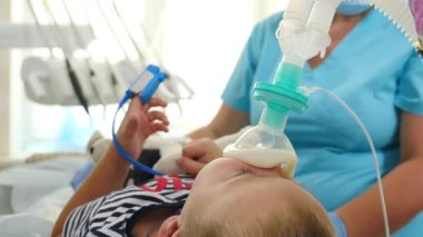 Anestezi gören çocuk. Modern diş kliniğinde genel narkoz altında diş hekimliği. Kimliği belirsiz bir çocuk. Nabız oksimetresi parmaklarında. Ameliyat odasında oksijen maskesi soluyor.