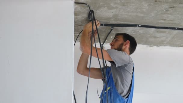 Installazione di cavi elettrici sul soffitto dell'appartamento. Impostazione del sistema di cavi elettrici. Elettricista che ripara fili. Miglioramento della casa. Elettricista mette cavo elettrico in edificio prefabbricato. 4 k — Video Stock