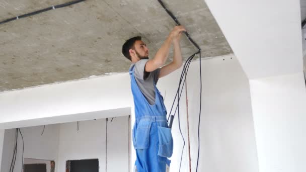 Installatie van elektrische bedrading op het plafond van het appartement. Elektrische kabel systeem instelling. Elektricien repareert draden. Huisverbetering. Elektricien zet elektrische kabel in geprefabriceerd gebouw. 4 km — Stockvideo