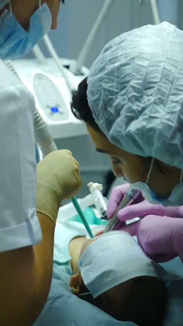 Zahnbehandlung bei Kindern unter Vollnarkose. Zahnarzt behandelt Zähne von Mädchen. Vertikale Aufnahmen. Team von professionellen Zahnchirurgen, die invasive Operationen an Patienten mit allgemeinen — Stockvideo