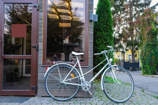 White old bicycle with the bottle dynamo device for the headlight on the front wheel. The bicycle is a decoration near a coffee shop. Empty sign on the glass door. Local tourism in Ukraine.