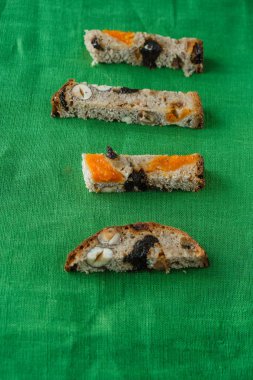 Fındıklı tatlı ekmeği dilimleri, kuru erik ve yeşil bir tuvalde kurutulmuş kayısılar. Ekmek tatma konsepti. Uzayı kopyala Üst Manzara. Dikey resim.