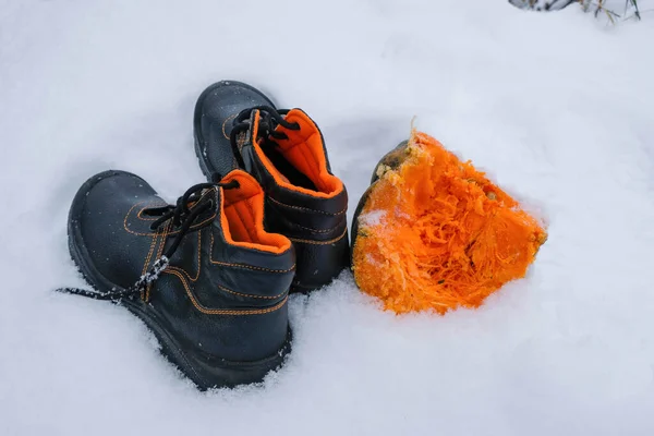 A pair of work boots with an orange lining for outdoor work. Comfortable work boots concept. Reflective surfaces. Snow background. Copy space.