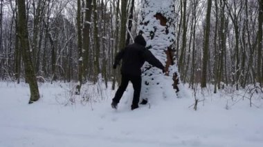 Kapüşonlu bir adam karla kaplı kudretli bir ağaca sarılır. Bir adamın üzerine kar yağar. Günaydın kış ormanı. İnsanlar ve doğa.