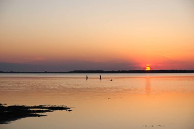 Günbatımı arka planında insan siluetleri. Sudaki güneşli yol. Svityaz Gölü, Ukrayna. Boşluğu kopyala.