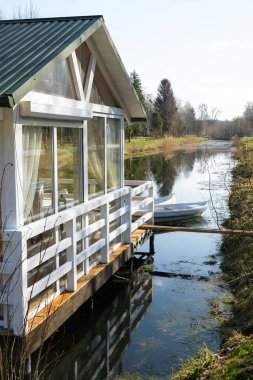 Baharın güneşli sabahında, suyun üzerindeki beyaz kulübe. Beyaz tekneler. Dikey resim.