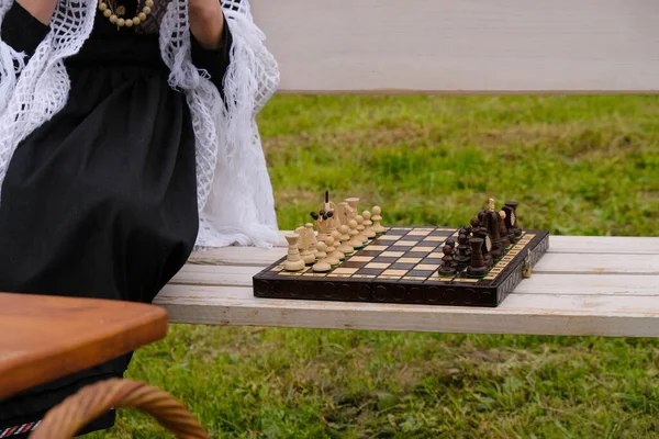 Vintage wooden chess board on a park bench. Girl in retro clothes plays chess. Retro picnic in Ukraine.