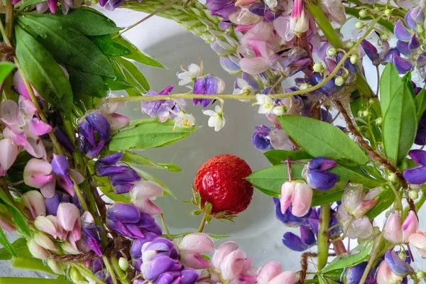 Strawberries and colorful flowers float in cool water. Summer fresh concept.