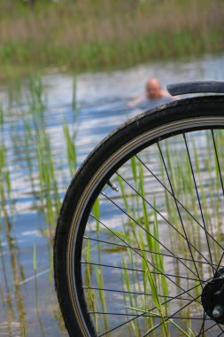 Bicycle wheel on a forest lake background. Athletic man swims in the lake. Vertical image.