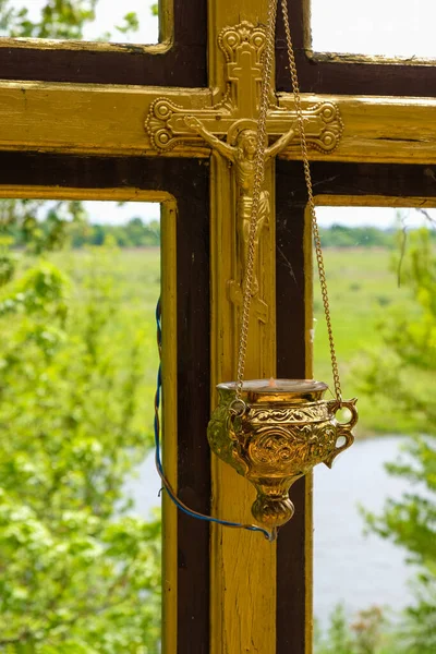 Orthodox pendant lamp on a wooden cross with a crucifix on a natural background. Golden church color.