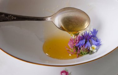 Natural honey flows from a spoon on flowers in a cup. Honey with meadow flowers in a white porcelain cup.