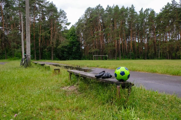 Green soccer ball and soccer boots on the forest stadium background in the morning after the rain. Bicycle in view. Ukraine.