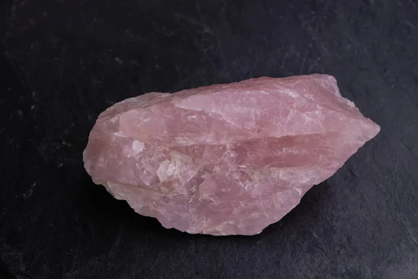 Pink quartz mineral isolated on the black natural slate. Close up. Copy space.
