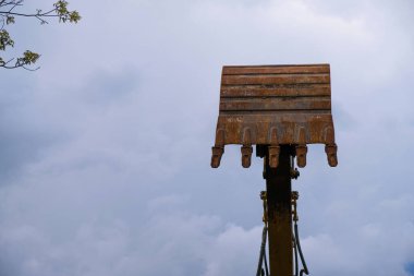 Bulutlu arka planda kazı kovası. Ağır makine kiralama konsepti. Boşluğu kopyala.