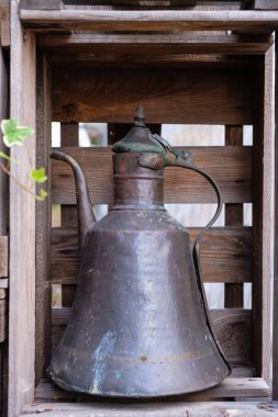 Pirinçten ya da bakırdan yapılmış eski bir çaydanlık bahçe süsü olarak ahşap bir kutuda duruyor. Dikey resim.