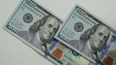 100 dolarlık banknotlar tek tek beyaz bir yüzeye yerleştiriliyor. Üniformalı ışıklandırma. Minimalizm. İş, hesaplamalar, kâr.