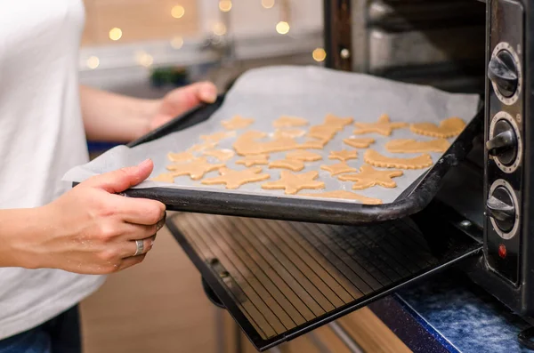女性の手はオーブンで生の生姜クリスマスクッキーとベーキングシートを置きます — ストック写真