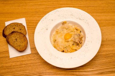 Lokantadaki beyaz tabakta yumurta sarısı ile iştah açıcı carbonara makarnası, ahşap masada iki parça ekmek.