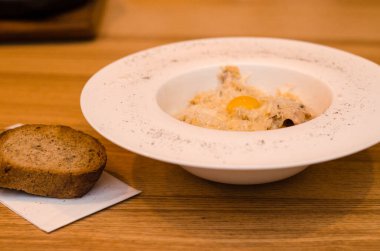 Lokantadaki beyaz tabakta yumurta sarısı ile iştah açıcı carbonara makarnası, ahşap masada iki parça ekmek.