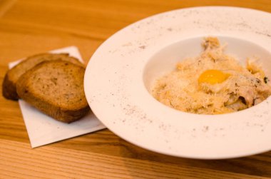 Lokantadaki beyaz tabakta yumurta sarısı ile iştah açıcı carbonara makarnası, ahşap masada iki parça ekmek.
