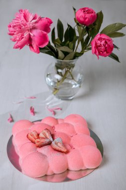 Çilekli kremalı pasta masanın üzerinde duruyor. Bir buket pembe şakayık..