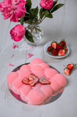 Çilekli kremalı pasta masanın üzerinde duruyor. Bir buket pembe şakayık..