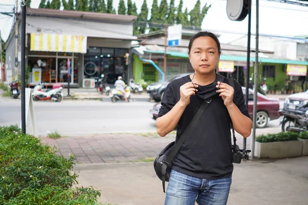 身穿黑色T恤和吉恩长裤的亚裔男子 身穿黑色面具 站在蓝色的泰国商业大厦和乡村道路上 — 图库照片