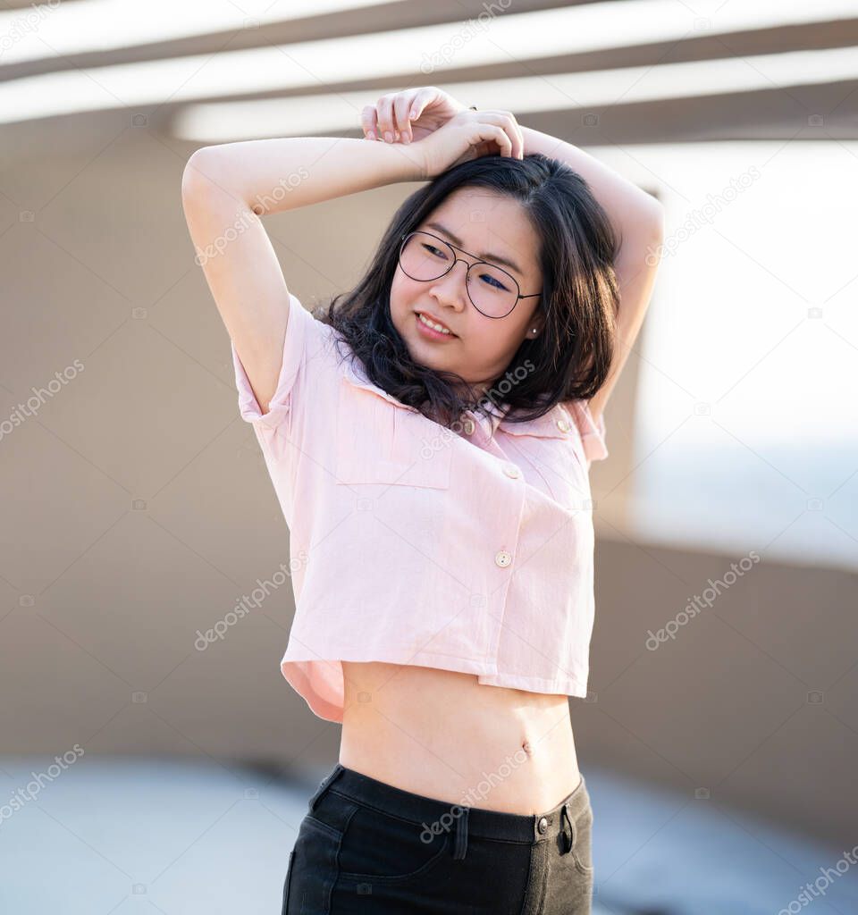 Beautiful Glasses Asian woman raise her hand up and poses for an image at outdoor rooftop building environment.
