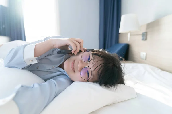Asian young glasses woman talk to the mobile phone while lie on her side on the bed in the morning.