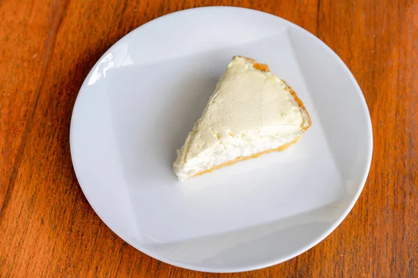 Ahşap masadaki tabakta üzerinde hiçbir şey olmadan hindistan cevizi kremalı turtayı temizle. Güneş ışığında çekim yapmak..