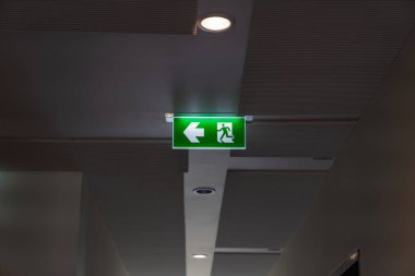 Tavandan sarkan yeşil bir yangın merdiveni, bir çıkış işareti yeşil ışık kutusu, koşan bir adam ve güvenlik ve tahliye için bir ok..