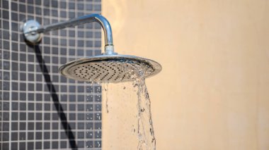 Su yuvarlak metal bir duş başlığından fayanslı bir duvara doğru akar, güneş ışığı su dokusunu ve açık havayı aydınlatır..