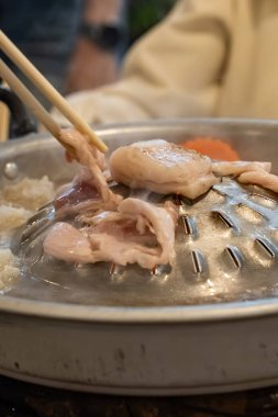 Dilimlenmiş et ve sebzeler et suyu ve buharla dolu metal bir ızgarada pişirilirken merkez de eti kızartır..