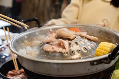 Dilimlenmiş et ve sebzeler et suyu ve buharla dolu metal bir ızgarada pişirilirken merkez de eti kızartır..