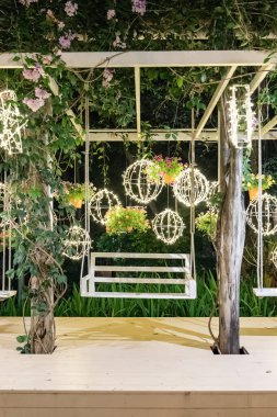 A white garden pavilion glows with hanging lights shaped like spheres and stars, while flowers and vines decorate the structure in the quiet night garden.