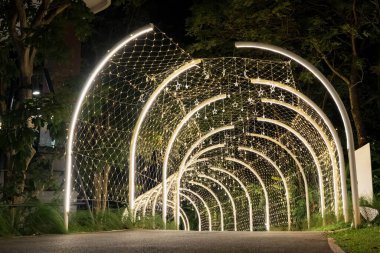 Curved white beams form an illuminated tunnel accented with hanging lights, and the structural lines create a clean pattern against the dark background.