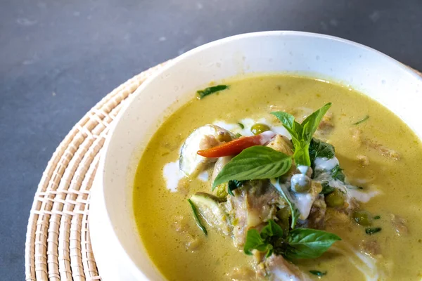 Yeşil Curry 'ye yaklaş, üzerine biber ve fesleğenle süslenmiş tavuk hasırlı krem rengi minder üzerine beyaz kase ile servis edildi..