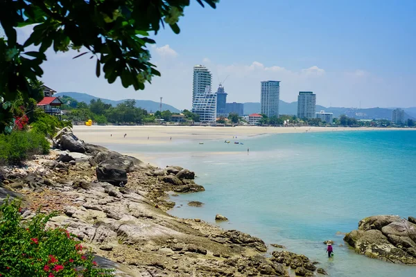 Hua Hin, Tayland 'daki sakin sahil manzarası, ufukta gökdelen manzarası ve mavi gökyüzü. Plaj kayaları ve tropikal bitkiler.