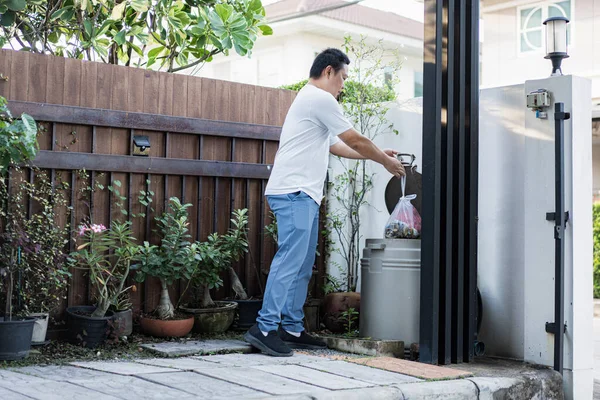 Bir adam evinin önündeki çöpleri düzgünce atıyor. Basit bir an, günlük hayatta sorumluluk ve farkındalığı yansıtır..