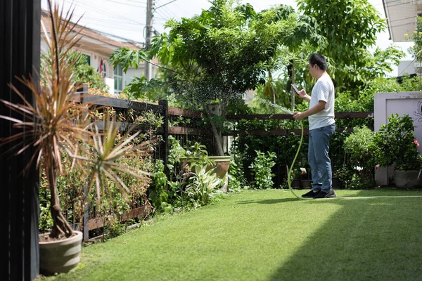 Bir adam güneşli bir bahçede akıllı telefonunu kontrol ederken bitkileri sular. Sahne modern yaşam ve doğa arasındaki dengeyi gösteriyor..