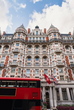 Klasik İngiliz mimarisi, kırmızı tuğlalı binalar ve bulutlu gökyüzünün altındaki tarihi cepheleriyle geleneksel bir Londra caddesini çiziyor..