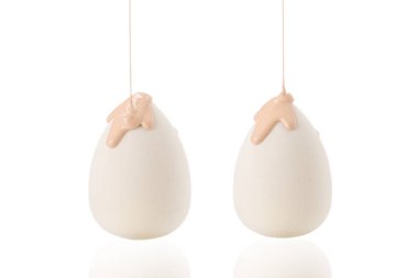 Beyaz arka planda izole edilmiş yeni beyaz süngerin üzerine dökülen sıvı bej makyaj vakfı