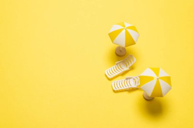 Sarı arka planda iki güneşlik ve kırmızı bir şemsiye. Boşluğu kopyala.