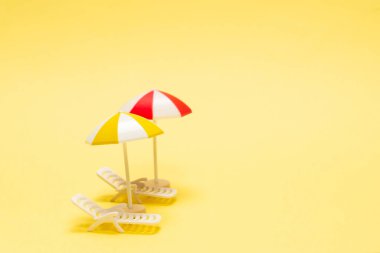 Sarı arka planda iki güneşlik ve kırmızı bir şemsiye. Boşluğu kopyala.