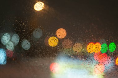 Yağmur damlaları ve ışıklarla bulanık arkaplan.
