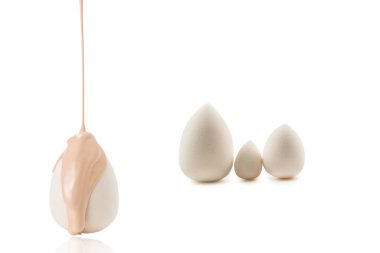 Beyaz arka planda izole edilmiş yeni beyaz süngerin üzerine dökülen sıvı bej makyaj vakfı