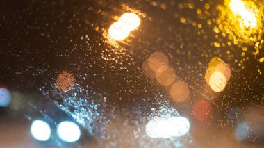 Yağmur damlaları ve ışıklarla bulanık arkaplan.